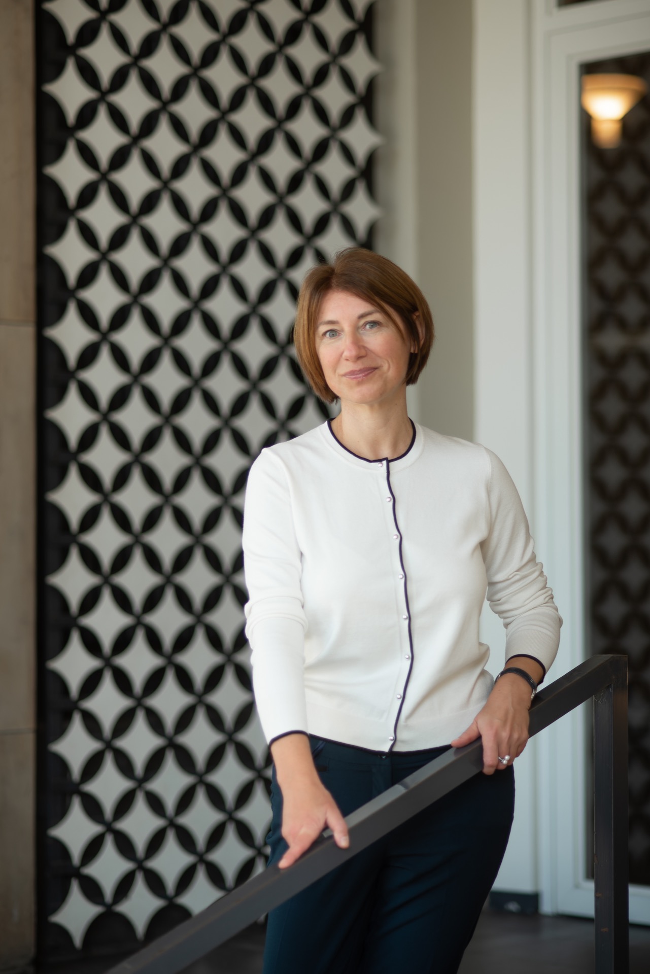 Business-Frau mit bob frisur in weissem jacket mit schwarzen rändern vor schwarzem hintergrund mit weissen sparkles, hält die hände an einem geländer